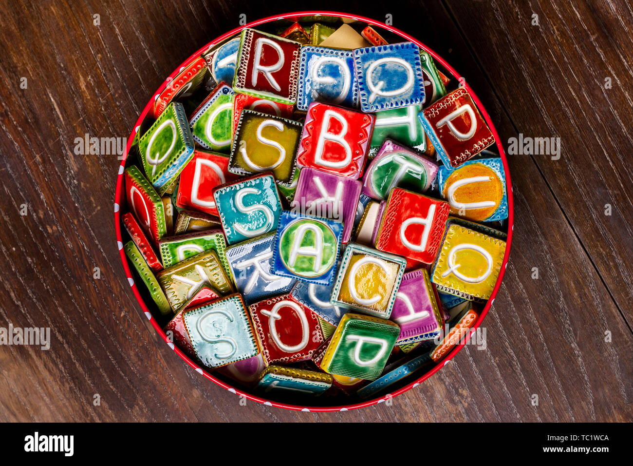 Barattolo di latta pieno di colorate piastrelle di ceramica con lettere  sulla texture di legno Foto stock - Alamy