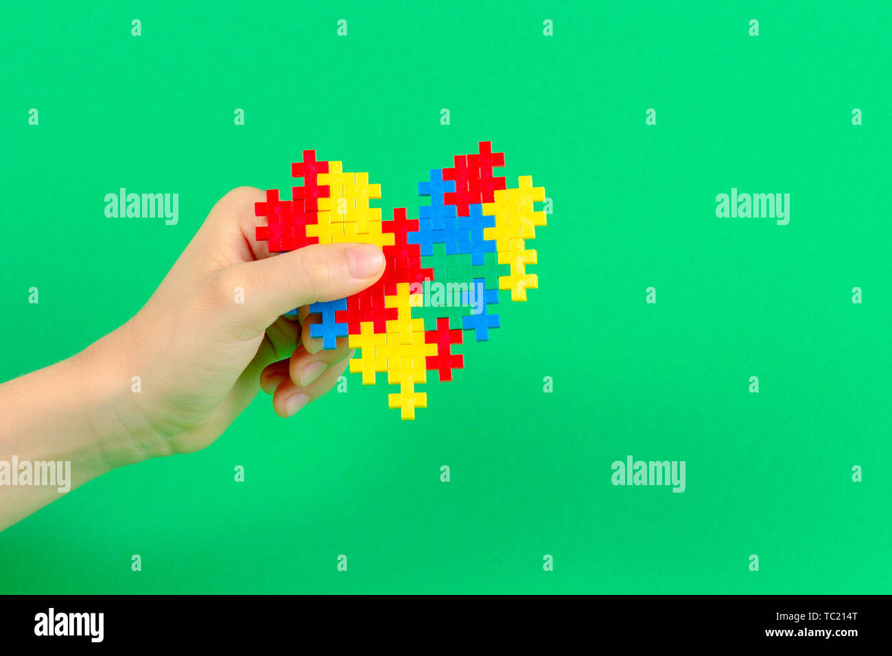 Bambino mano azienda cuore colorati su sfondo verde. Mondo autismo consapevolezza giorno di concetto Foto Stock