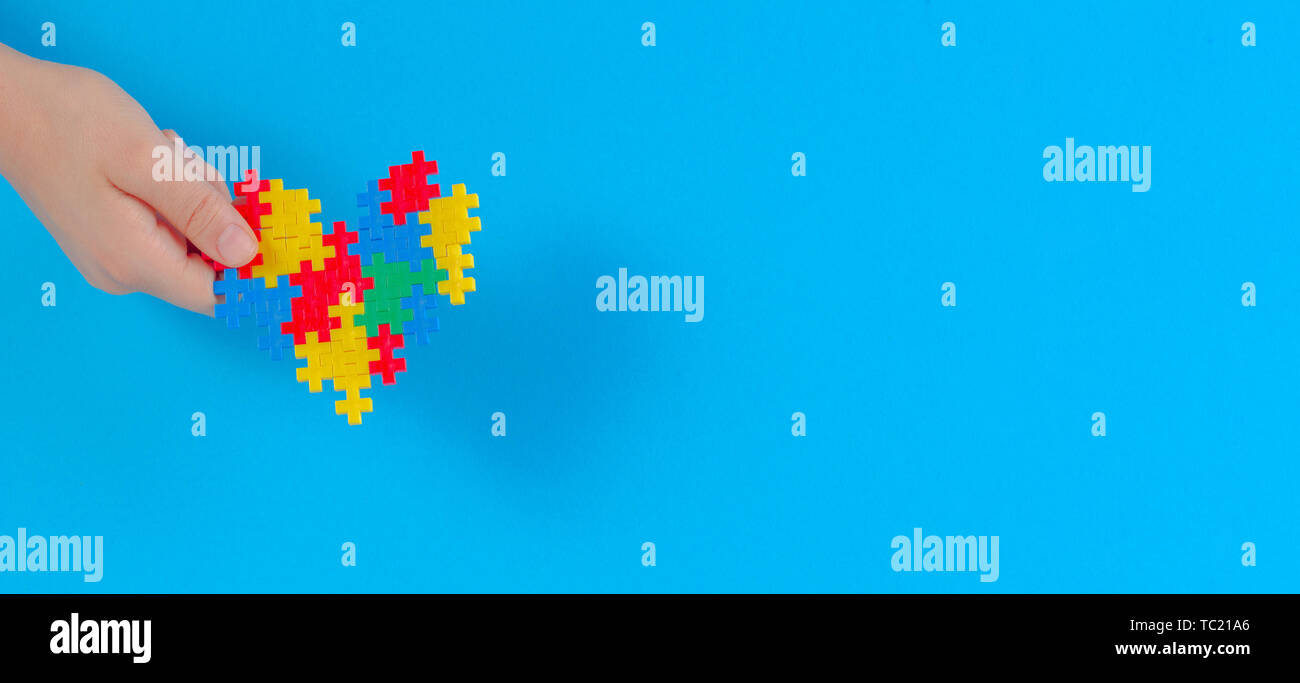 Bambino mano azienda cuore colorati su sfondo blu. Mondo autismo consapevolezza giorno di concetto Foto Stock