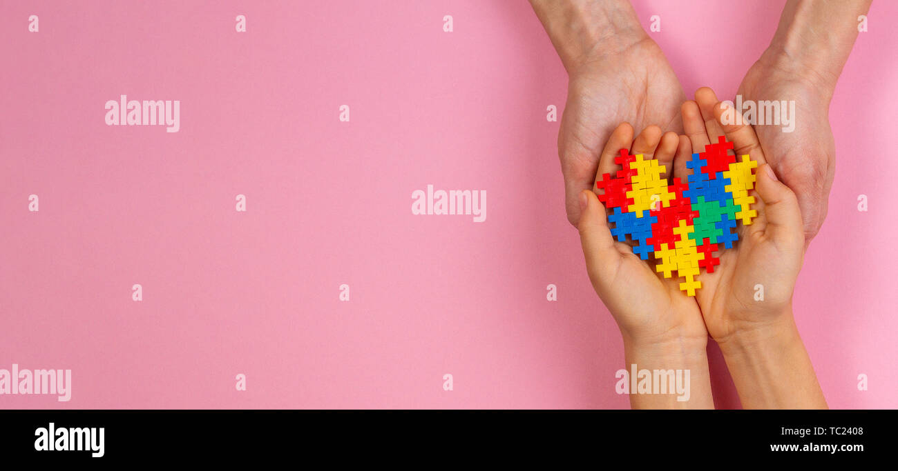 Adulto e bambino mani cuore colorati in rosa chiaro dello sfondo. Mondo autismo consapevolezza giorno di concetto Foto Stock