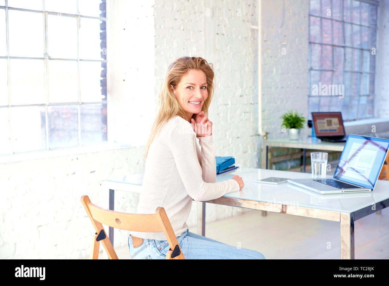 Ritratto di bella bionda imprenditrice seduto alla scrivania in ufficio dietro il suo computer portatile e funziona. Foto Stock