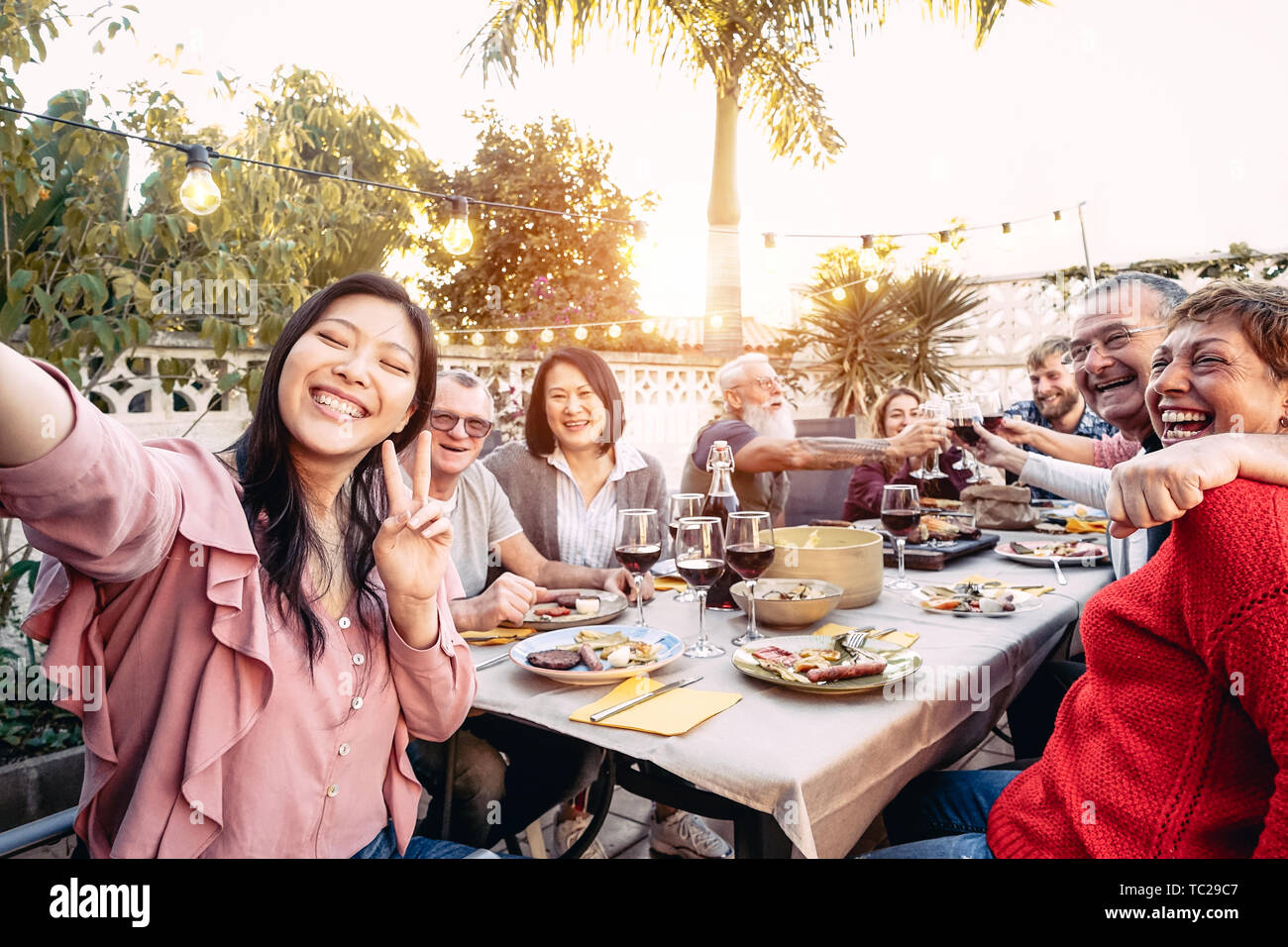 La famiglia felice il tifo e tostatura con red bicchieri di vino a cena outdoor - Persone con differenti età e di etnia divertendosi al barbecue party Foto Stock