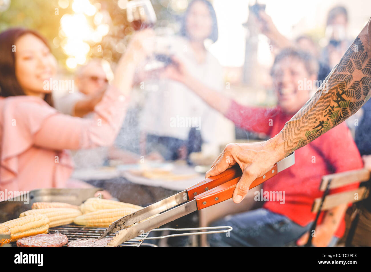 Tatuato senior uomo grigliare hamburger per la sua famiglia a cena a barbecue party - Close up mano maschio cottura su barbecue nel giardino Foto Stock