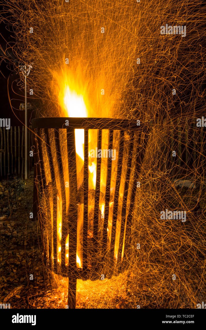 Un fuoco che brucia pit cestello in acciaio nelle tenebre fredda notte di ottobre in autunno con il fuoco scintille galleggianti intorno Foto Stock