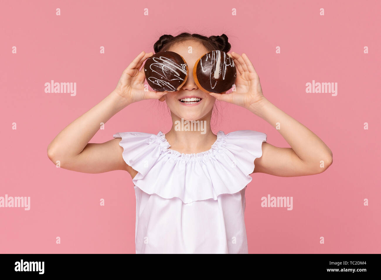 Poco sorridente ragazza che copre la sua gli occhi con ciambelle al cioccolato Foto Stock