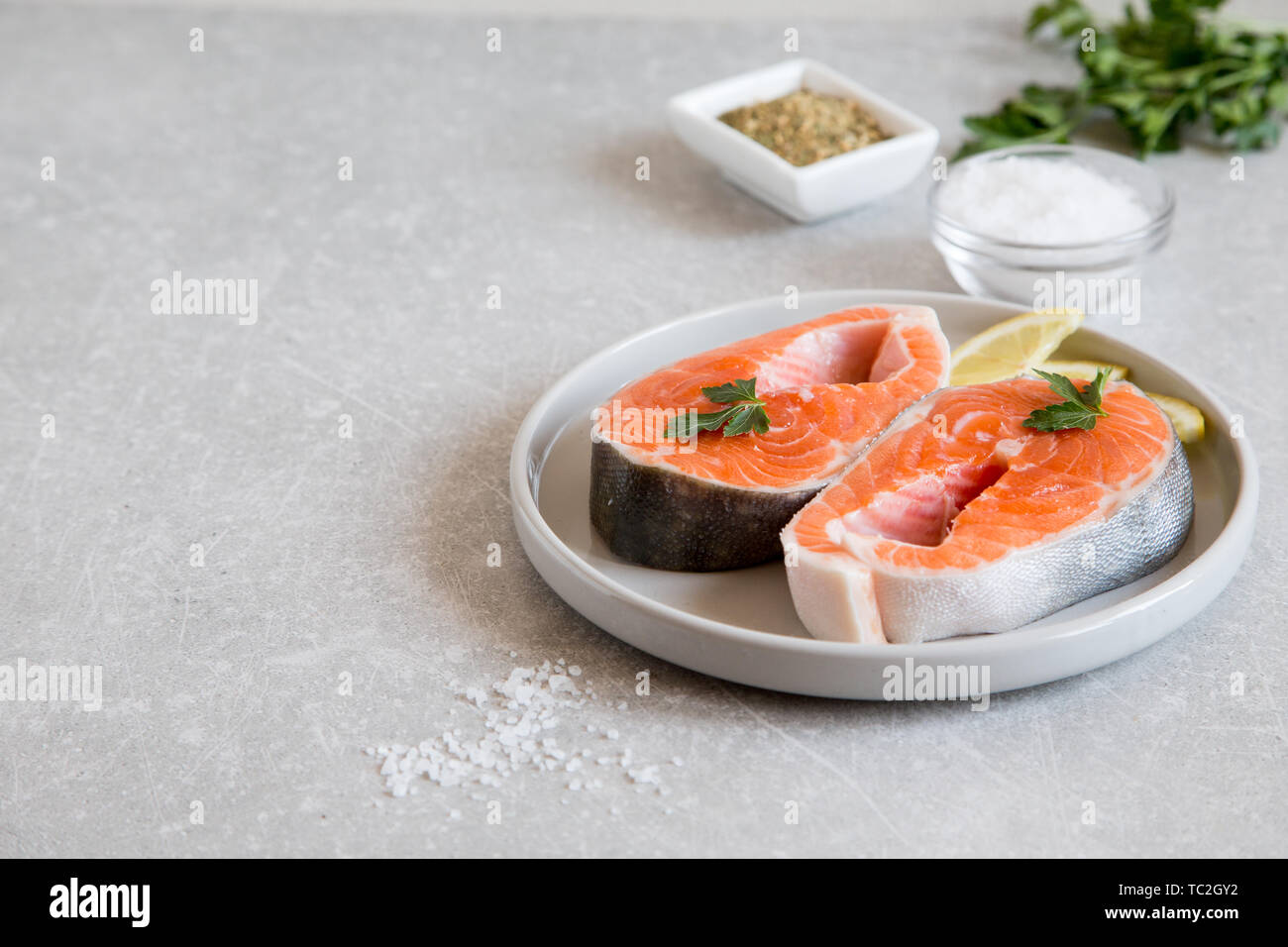 Pesce fresco salmone fresco bistecche con limone, spezie e sale in una piastra di luce. Foto Stock