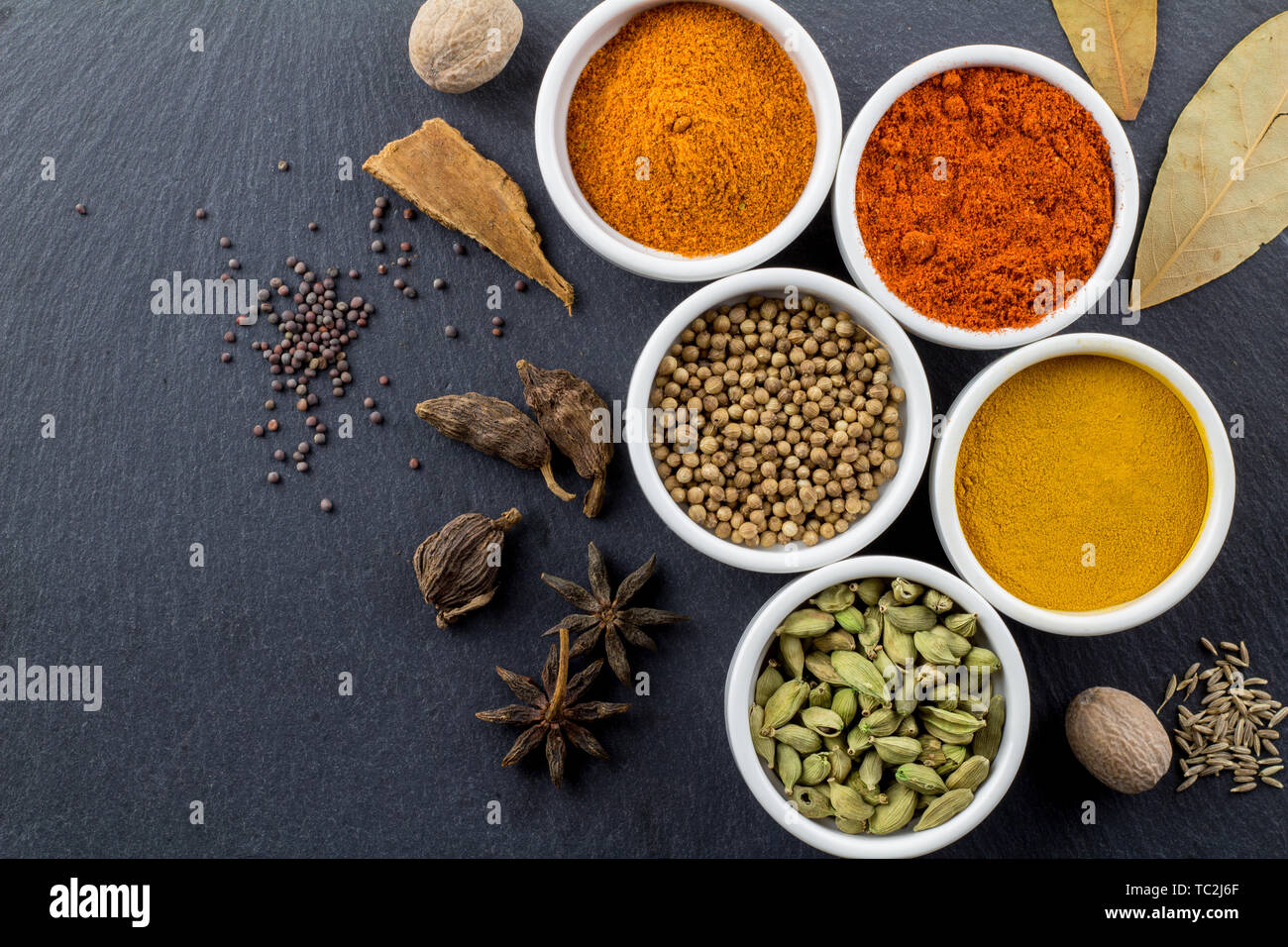 Le spezie in piccole ciotole bianco su nero ardesia background - Indian Spice top view foto con spazio per il testo Foto Stock