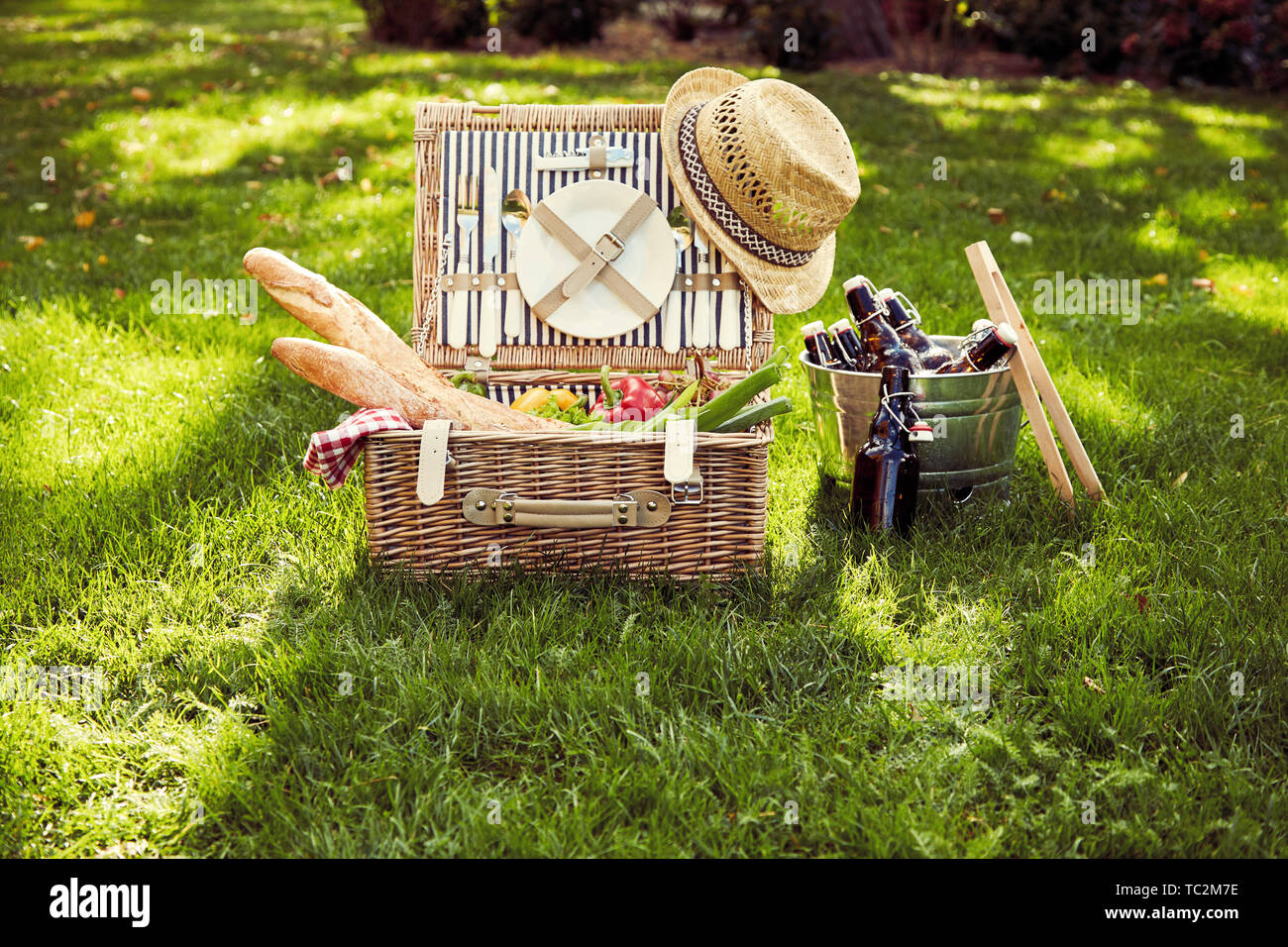 Vimini cesto da picnic con insalata vegetariana ingredienti, uve e baguette francesi al fianco di un argento wine cooler con bottiglie di birra in un vintage s Foto Stock