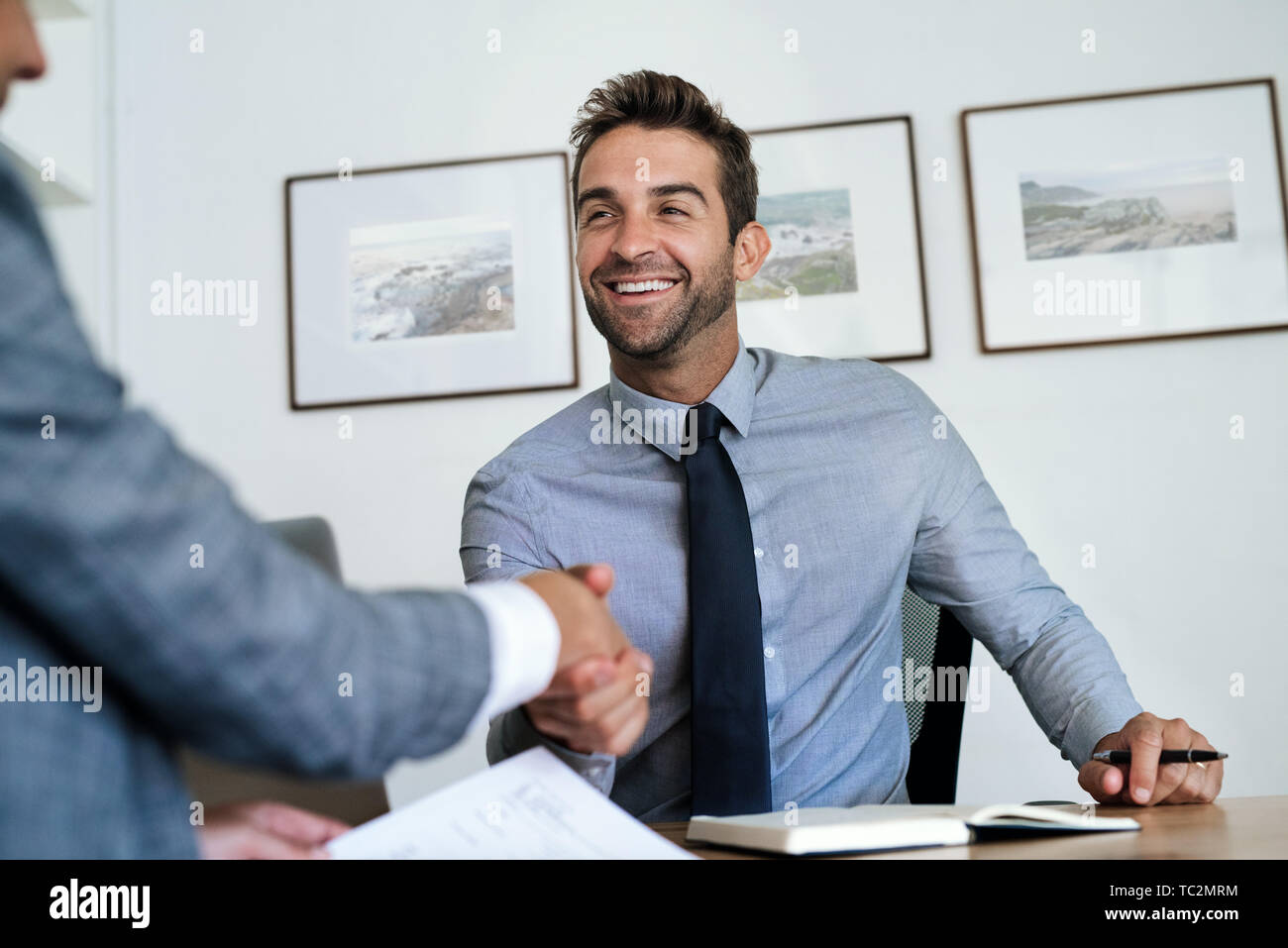 Manager seduto alla sua scrivania stringono le mani con un dipendente Foto Stock