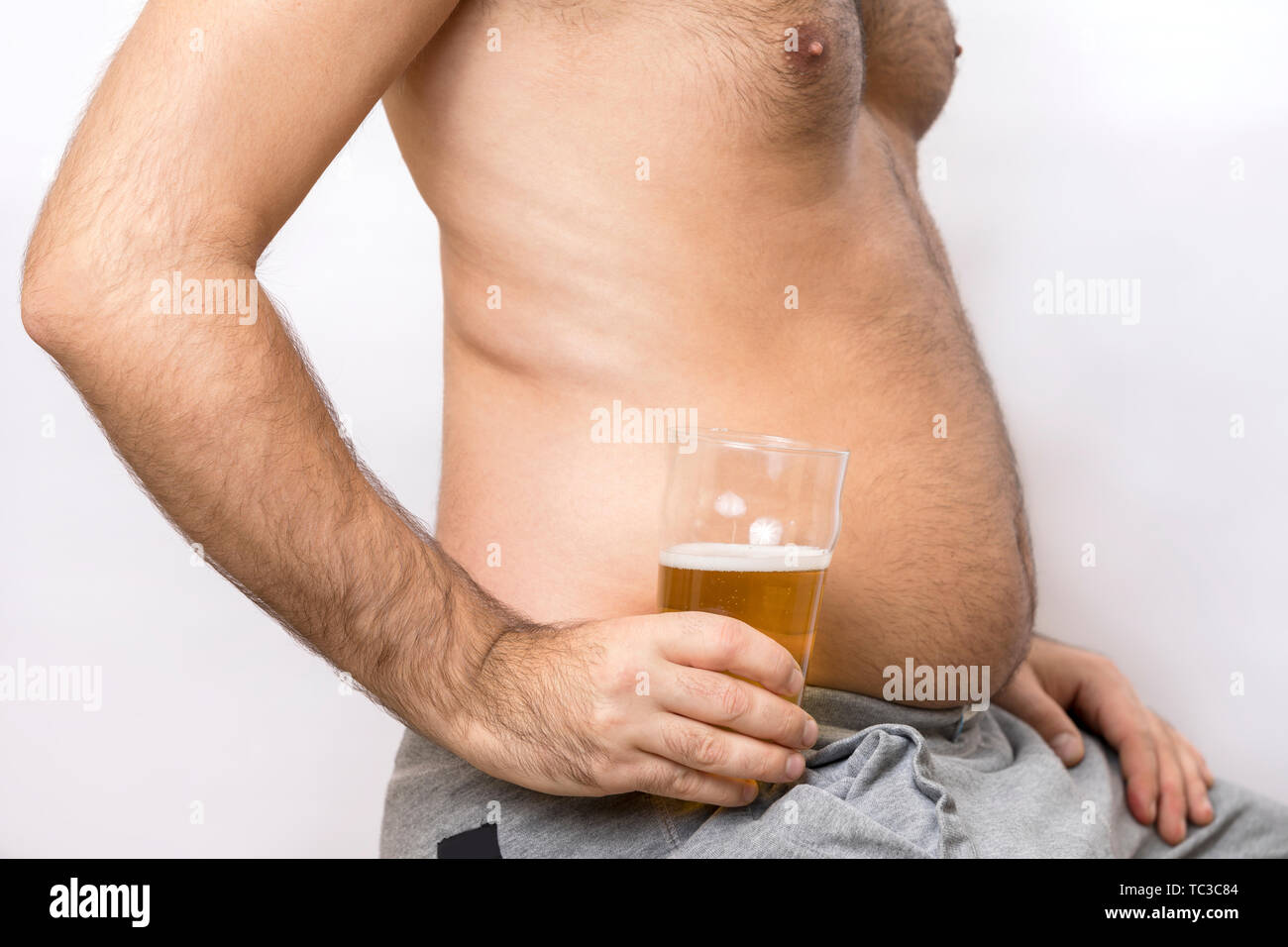 L'alcol Addicted uomo con un fat belly mantiene un bicchiere di birra Foto Stock