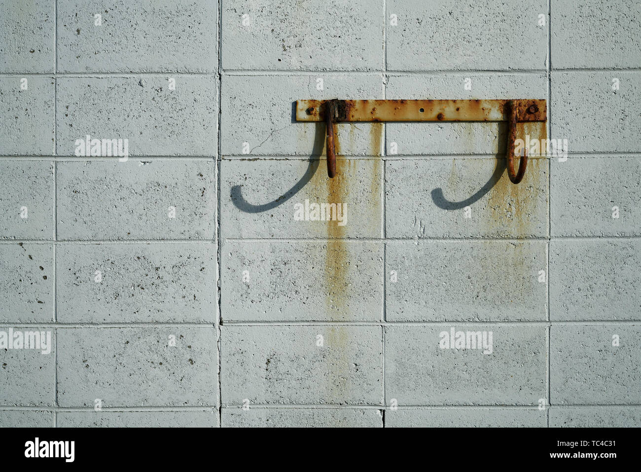 Rusty ganci su un macchiato di ruggine breeze blocco di muro sul fronte mare. Foto Stock