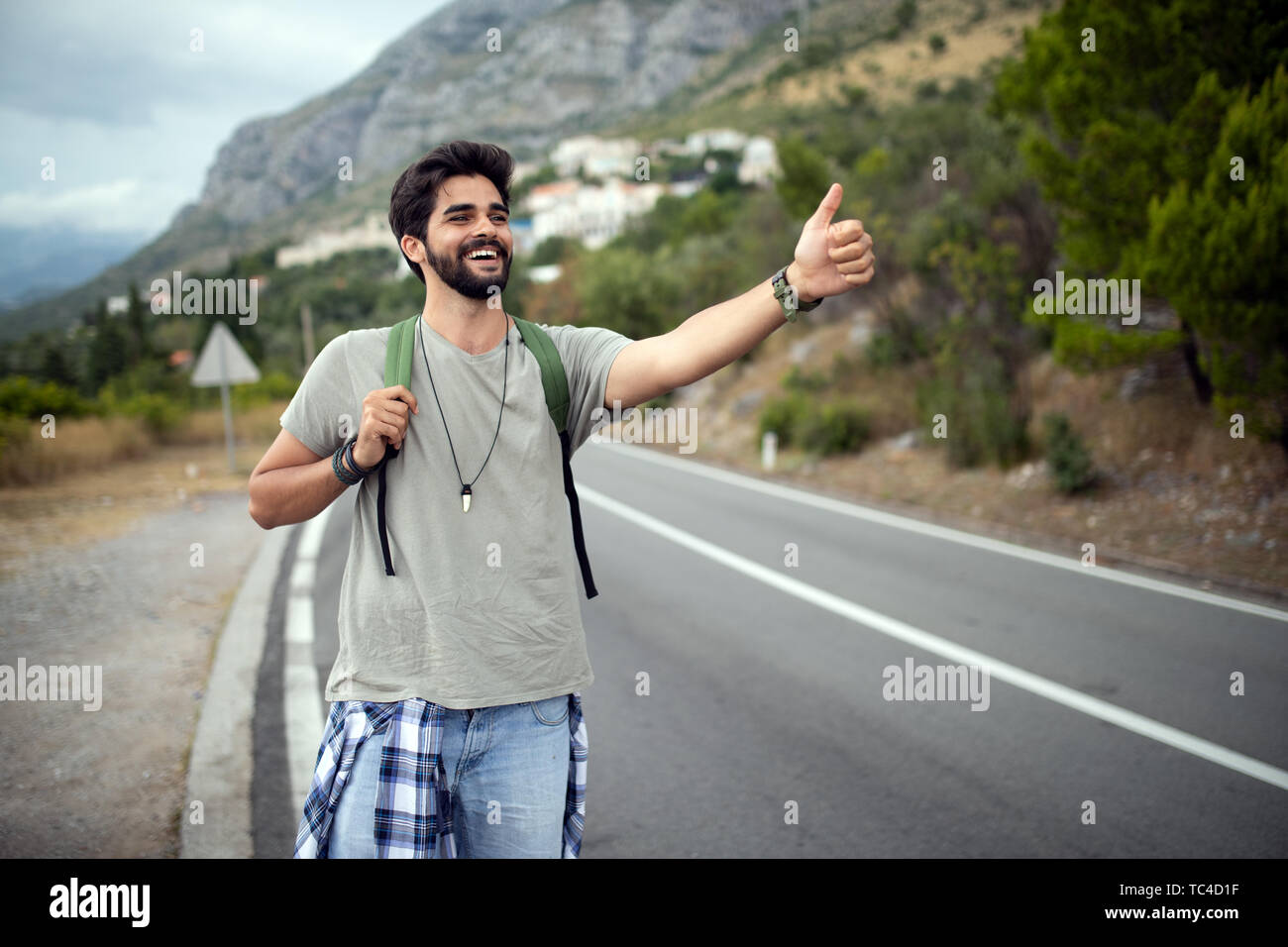 Autostop giovane viaggiatore uomo cercare di cattura auto su una strada forestale Foto Stock