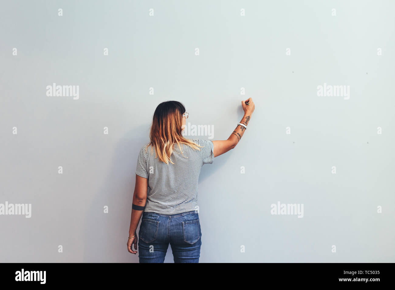 Vista posteriore di un illustratore facendo uno schizzo su una parete. Artista creativa la scrittura su una parete con un disegno penna. Foto Stock
