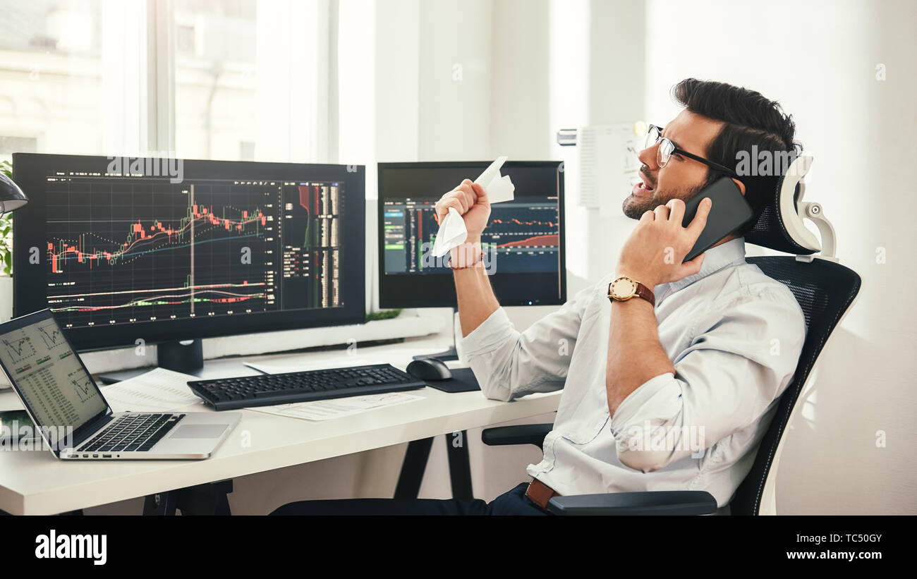 Nuovo fallimento... Premuto barbuto imprenditore o commerciante nel convenzionale e occhiali è di parlare con il cliente tramite smartphone e la sensazione di essere triste mentre è seduto in un ufficio moderno. Concetto di commercio. Concetto di investimento. Le moderne tecnologie Foto Stock