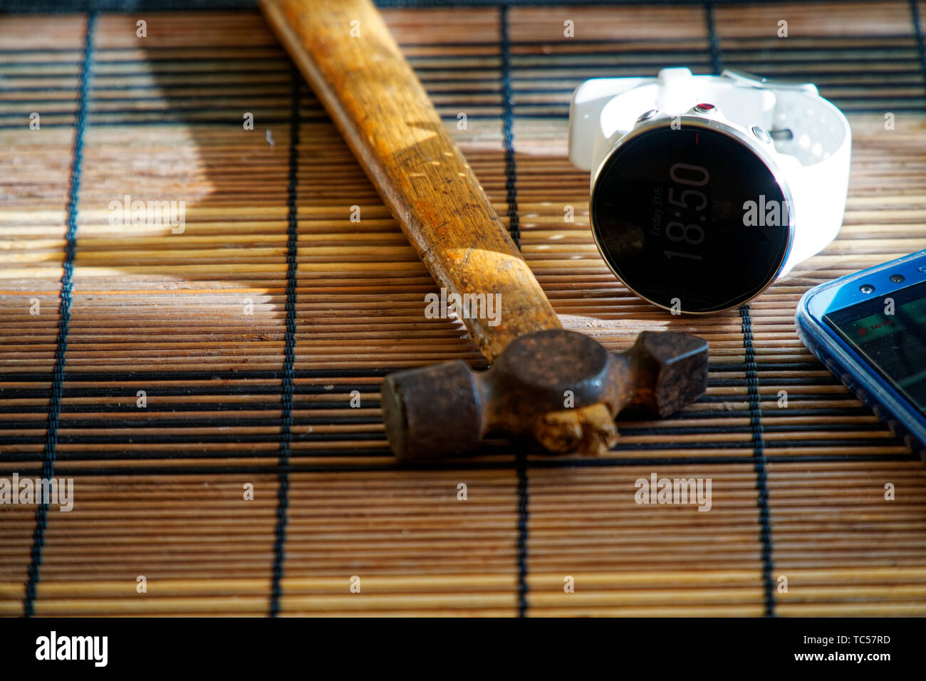 Orologio sportivo in colore bianco sul tavolo di legno, orologio intelligente per il running e fitness training. Martello con manico in legno su sfondo. Foto Stock