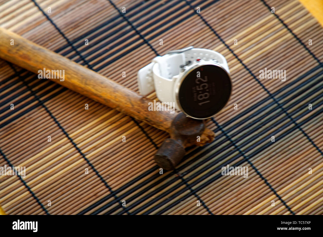 Orologio sportivo in colore bianco sul tavolo di legno, orologio intelligente per il running e fitness training. Martello con manico in legno su sfondo. Foto Stock