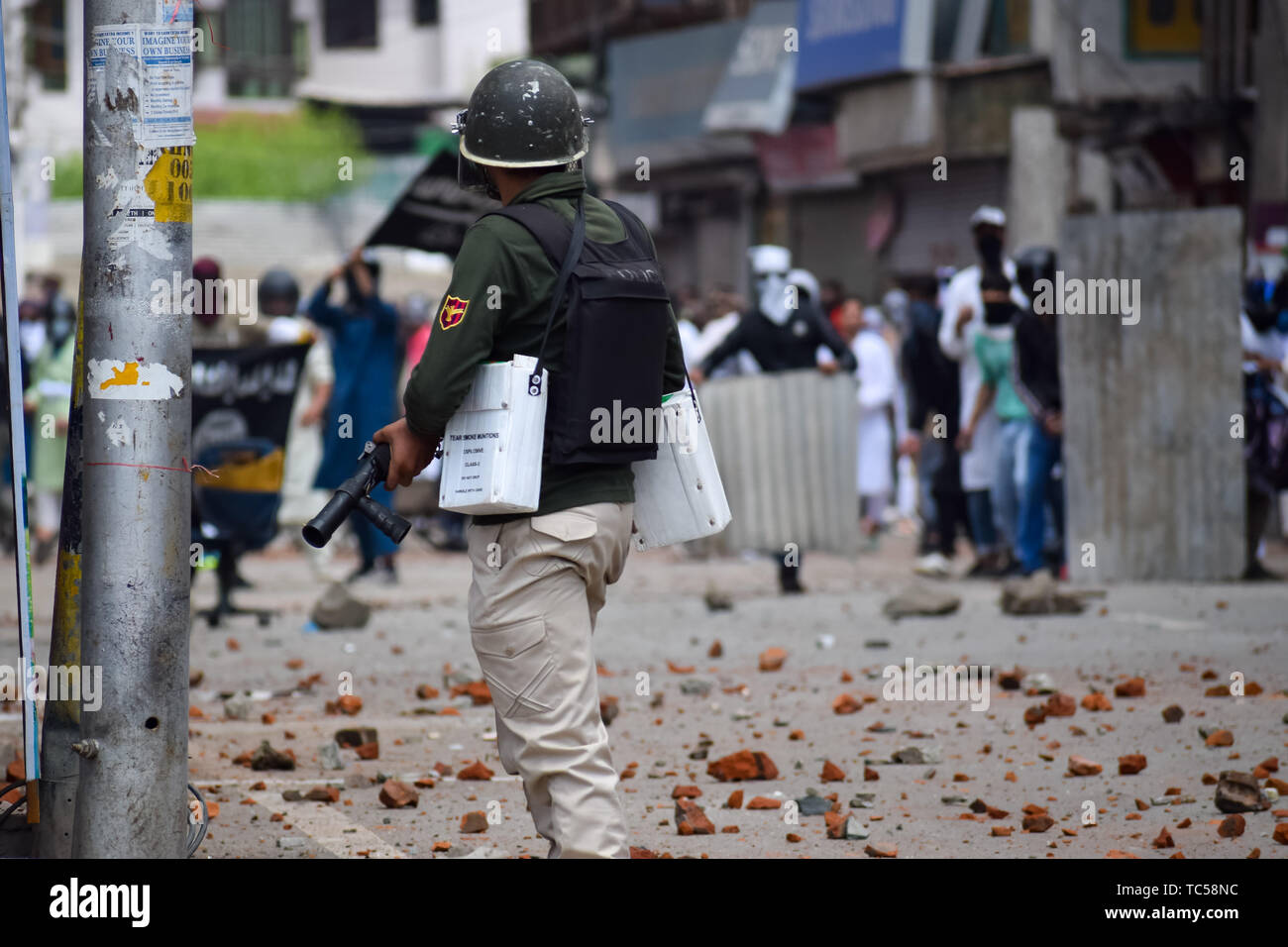 Un poliziotto indiano sorge sulla protezione come contestatori del Kashmir getta pietre durante gli scontri a Srinagar. Le forze indiane in Srinagar usato gas lacrimogeni fumogeni e proiettili per disperdere centinaia di manifestanti che hanno preso a strade dopo Eid-ul-Fitr preghiere per protestare contro la regola di indiana nella regione. Foto Stock