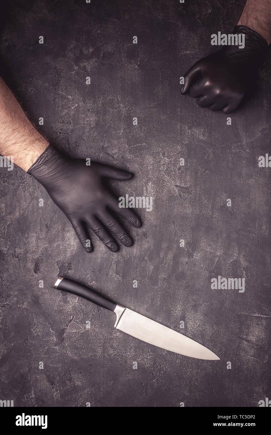 Grande coltello e mani maschio nero con guanti in lattice su sfondo scuro Foto Stock