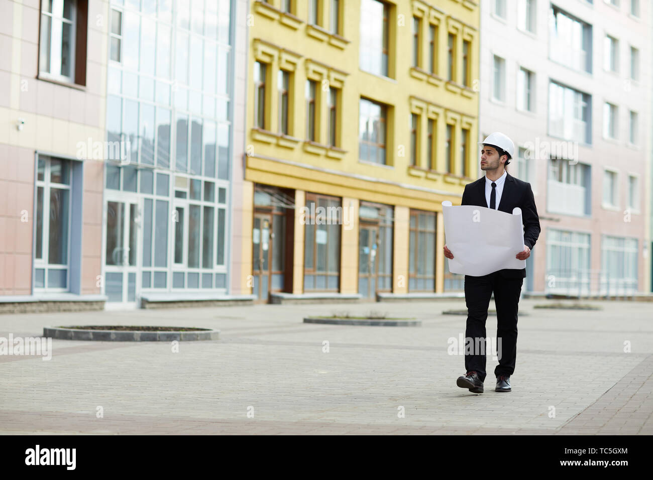 A piena lunghezza Ritratto di bello imprenditore mediorientale indossando hardhat camminando verso la telecamera al sito in costruzione, spazio di copia Foto Stock