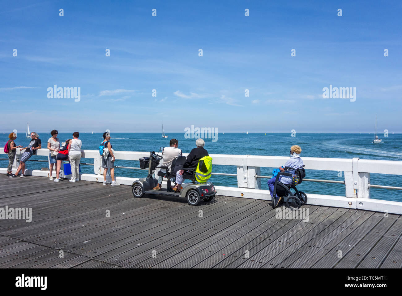 Donna disabile in carrozzina e per persone handicappate in duo due persona scooter di mobilità a guardare le barche a vela in mare dal jetty Foto Stock