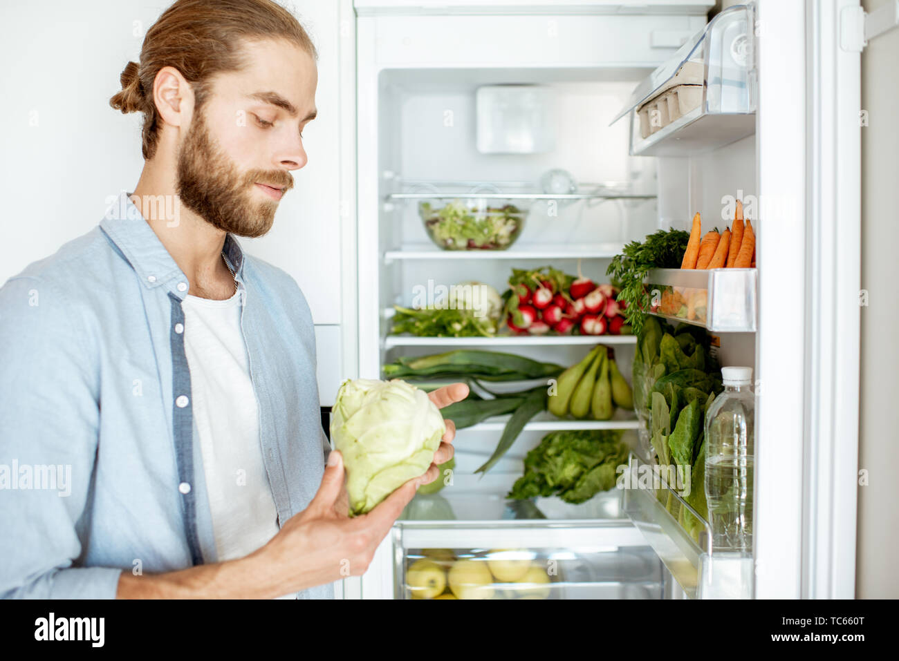 Giovane uomo vegano la scelta di cosa cucinare, tenendo le verdure fresche  dal frigorifero a casa Foto stock - Alamy