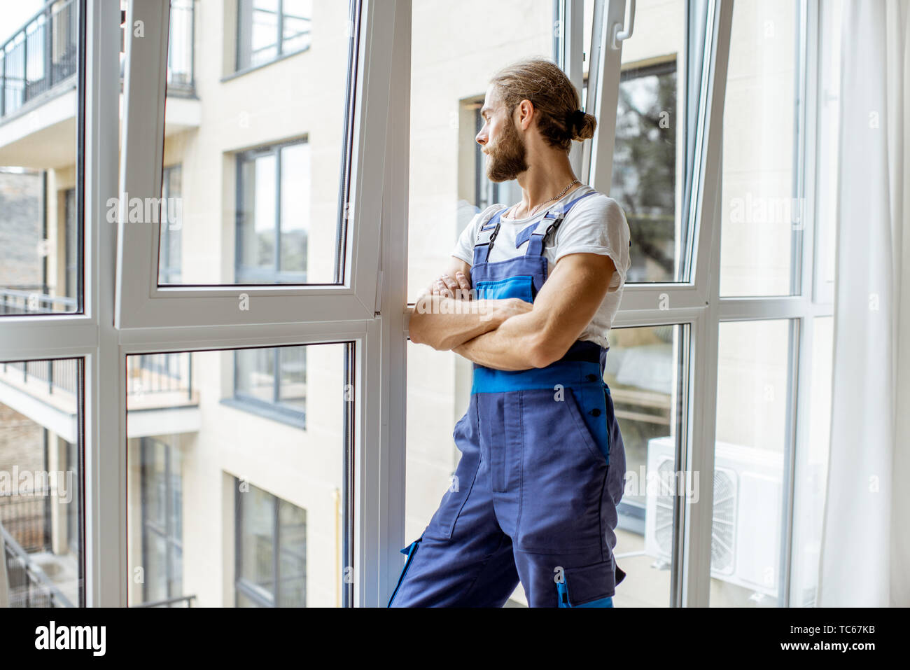Ritratto di un bel operaio in tuta in piedi vicino alla finestra nell'appartamento renovared Foto Stock