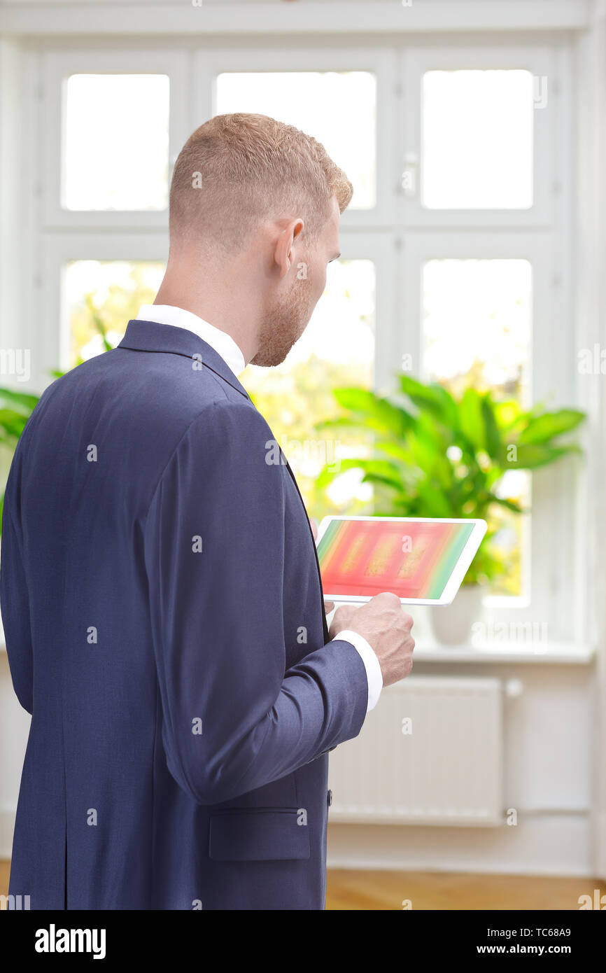 Maschio consulente energetico in una stanza di un vecchio edificio con un'immagine a raggi infrarossi di windows sul suo computer tablet Foto Stock