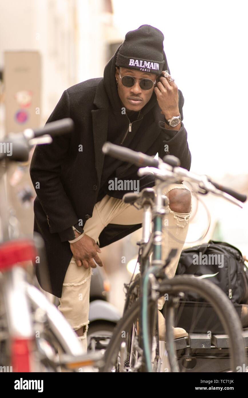 Moda uomo tra le biciclette che indossa felpa con cappuccio nero, vestiti  street style®, occhiali da sole e cappello dal marchio di moda Balmain, a  Monaco di Baviera, Germania Foto stock -