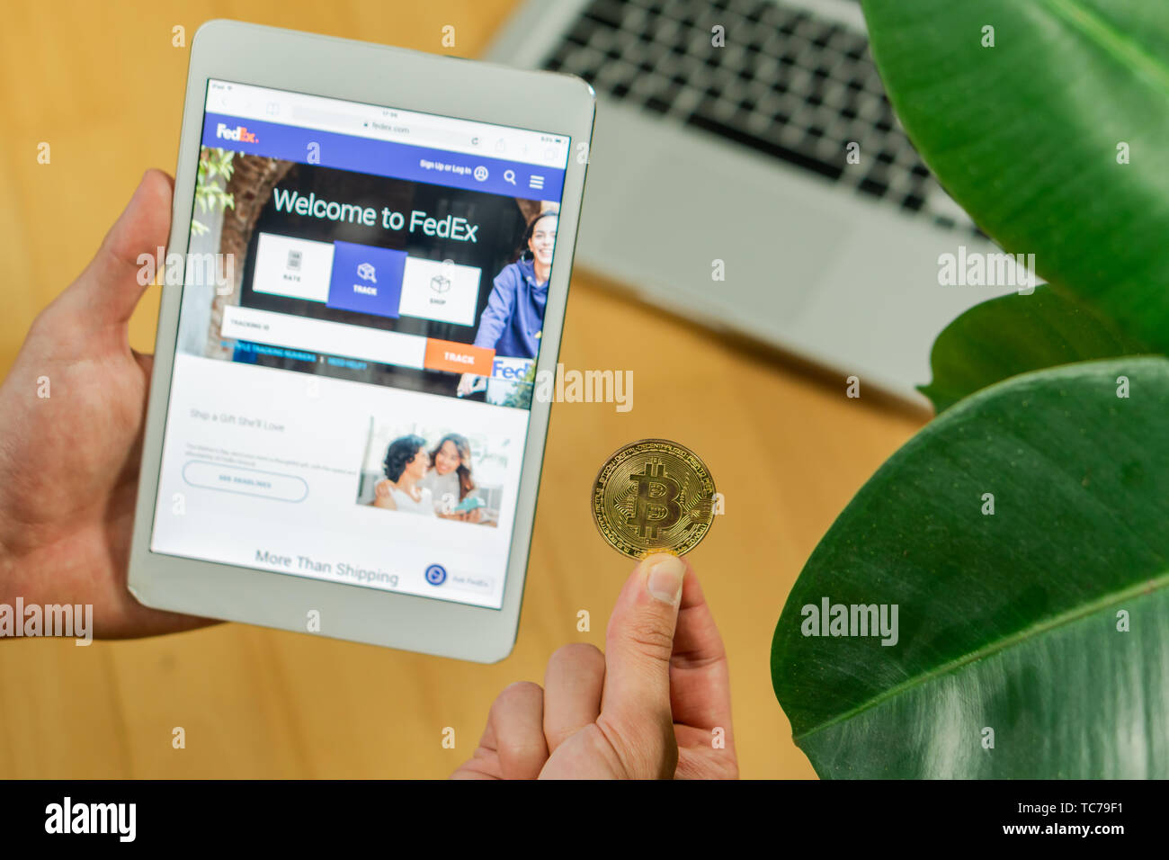 Lubiana, Slovenia 29.4.2019: Imprenditore azienda computer tablet con aperto il sito web di Fedex e moneta Bitcoin su una scrivania in ufficio Foto Stock