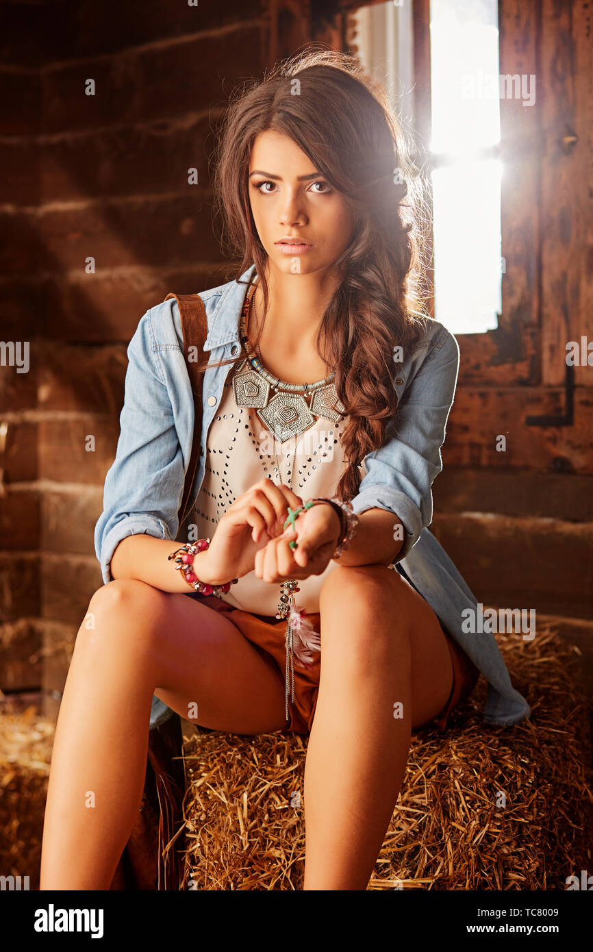 Leggy giovane ragazza seduta nel granaio, raddrizza il braccialetto sulla sua mano Foto Stock
