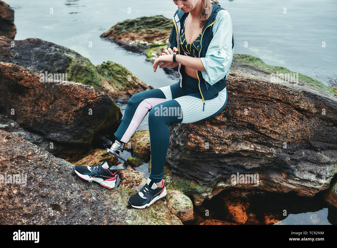 Ottimo allenamento. Foto ritagliata di atleti disabili donna in abbigliamento sportivo con gamba protesico il controllo dei risultati mentre è seduto sulla pietra. Sportivo disabili. Uno stile di vita sano. Sport concept Foto Stock