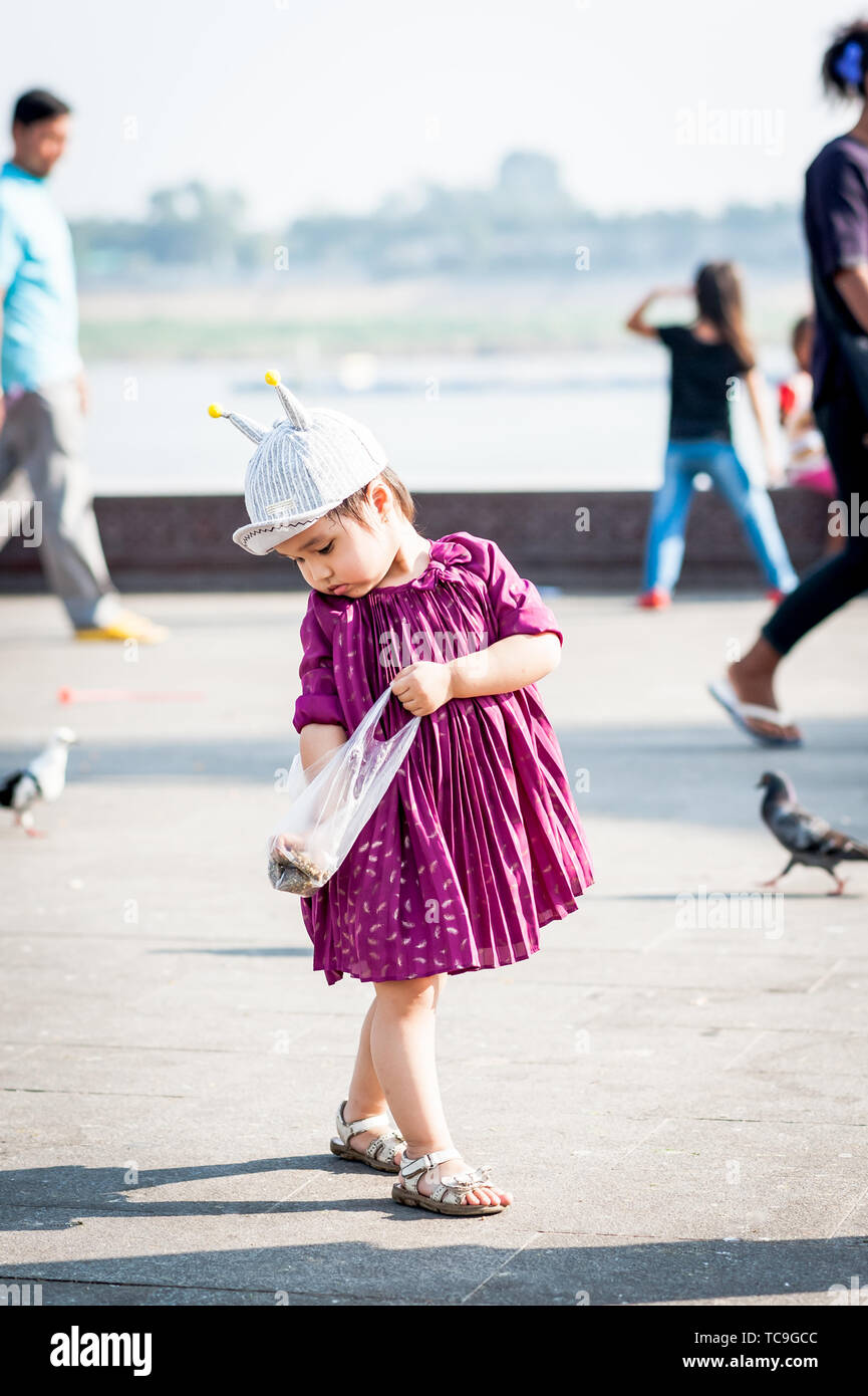 Una bambina carina si nutre felicemente dei piccioni lungo il lungomare di Phnom Penh, Cambogia. Foto Stock