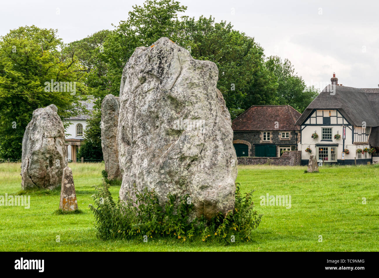 Le pietre della preistoria di Avebury Stone Circle con il villaggio di paglia, Pub Red Lion, in background. Foto Stock