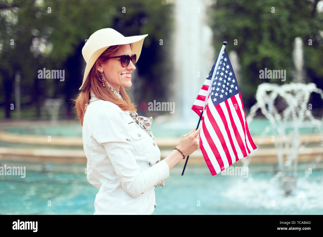 Giovane patriota woman in hat holding bandiera degli Stati Uniti nel parco presso la fontana, giorno di indipendenza, 4 Luglio Foto Stock