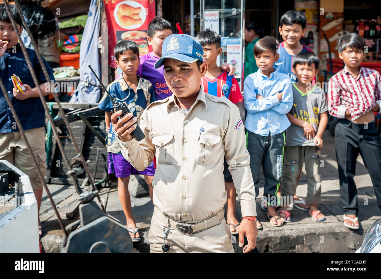 Un poliziotto cambogiano circondato da bambini di strada assiste ad una situazione in Cambogia la città di Phnom Penh. Foto Stock