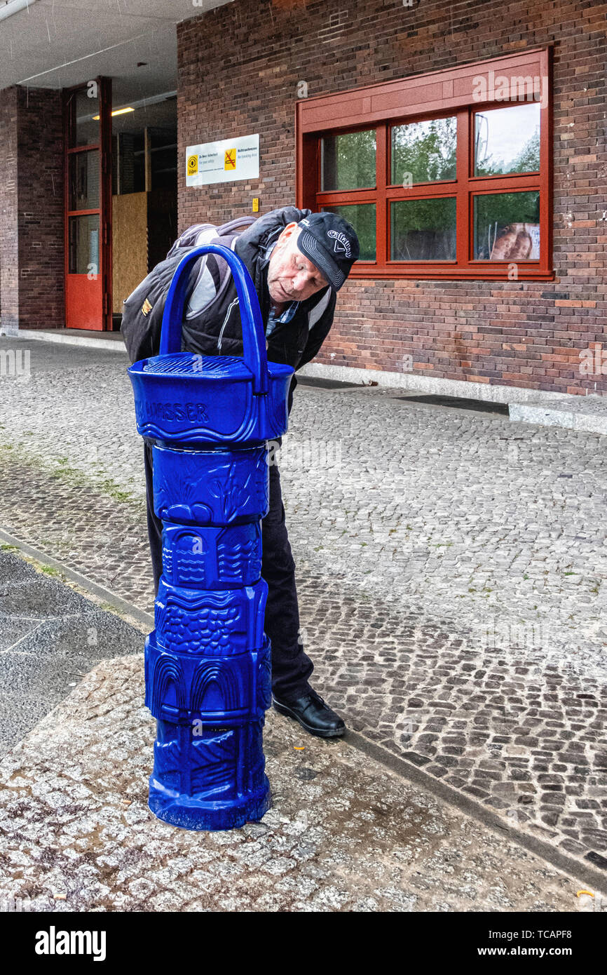 Senior uomo beve l'acqua dal vecchio blu fontana fuori Ruhleben U-Bahn stazione,quartiere Westend di Berlino Foto Stock