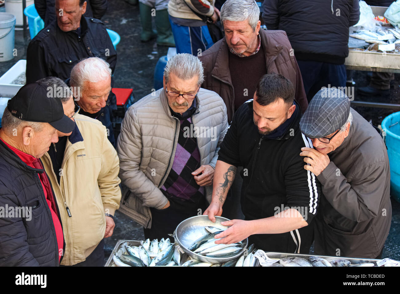 Catania, Sicilia, Italia - 10 Apr 2019: pescivendolo la vendita di pesce fresco su un tradizionale mercato del pesce. Gruppo di vecchi acquirenti è guardare e dare consigli. Popolare attrazione locale. Foto Stock