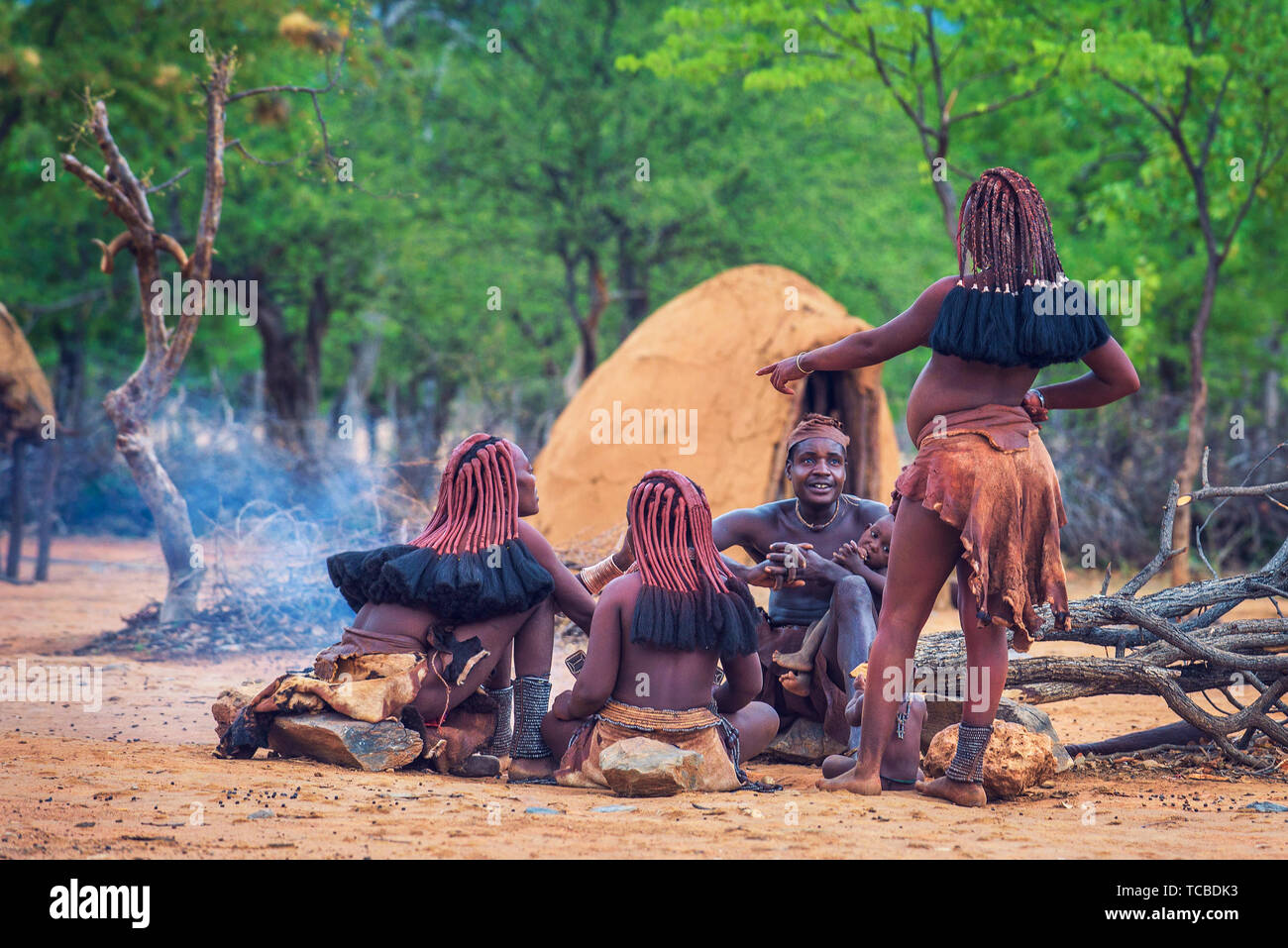 Le persone della tribù Himba seduti intorno al fuoco nel loro villaggio Foto Stock