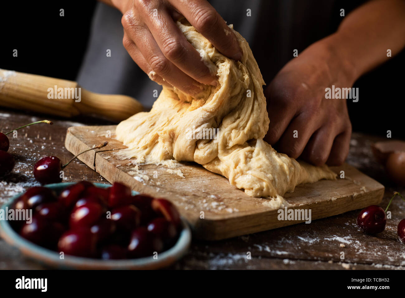 Primo piano di un giovane uomo caucasico impastando un pezzo di pasta per preparare una coca de cireres, una ciliegia dolce torta piatto tipico della Catalogna, Spagna, su un wo Foto Stock