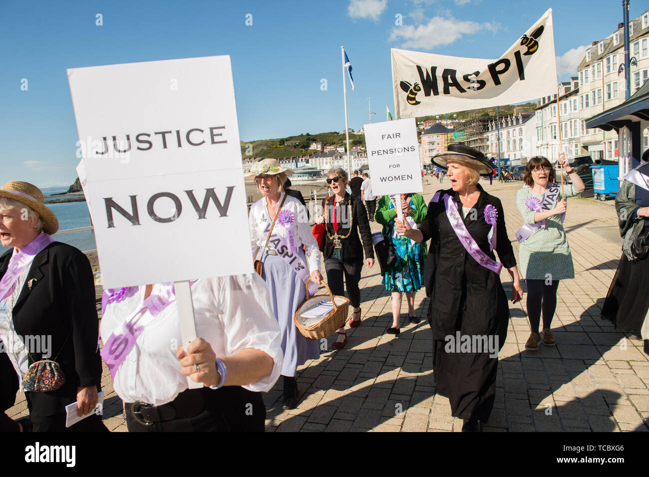 Aberystwyth Wales UK, giovedì 06 giugno 2019 un gruppo di targhetta porta-nonni nel loro 60s, vestito come suffragettes marciare lungo la passeggiata in Aberystwyth come parte di una nazione a livello di protesta contro il sollevamento dello stato dell'età di pensionamento per le donne . WASPI [donne contro la pensione statale ingiustizia] lottano per invertire la decisione di cambiare il pensionamento a 67 per le donne nate negli anni cinquanta . Ci sono 5.000 donne in Ceredigion nato negli anni cinquanta che hanno perso anni della loro pensione come risultato del governo della politica di accelerazione. La legittimità di tali modifiche è ora in fase di test Foto Stock