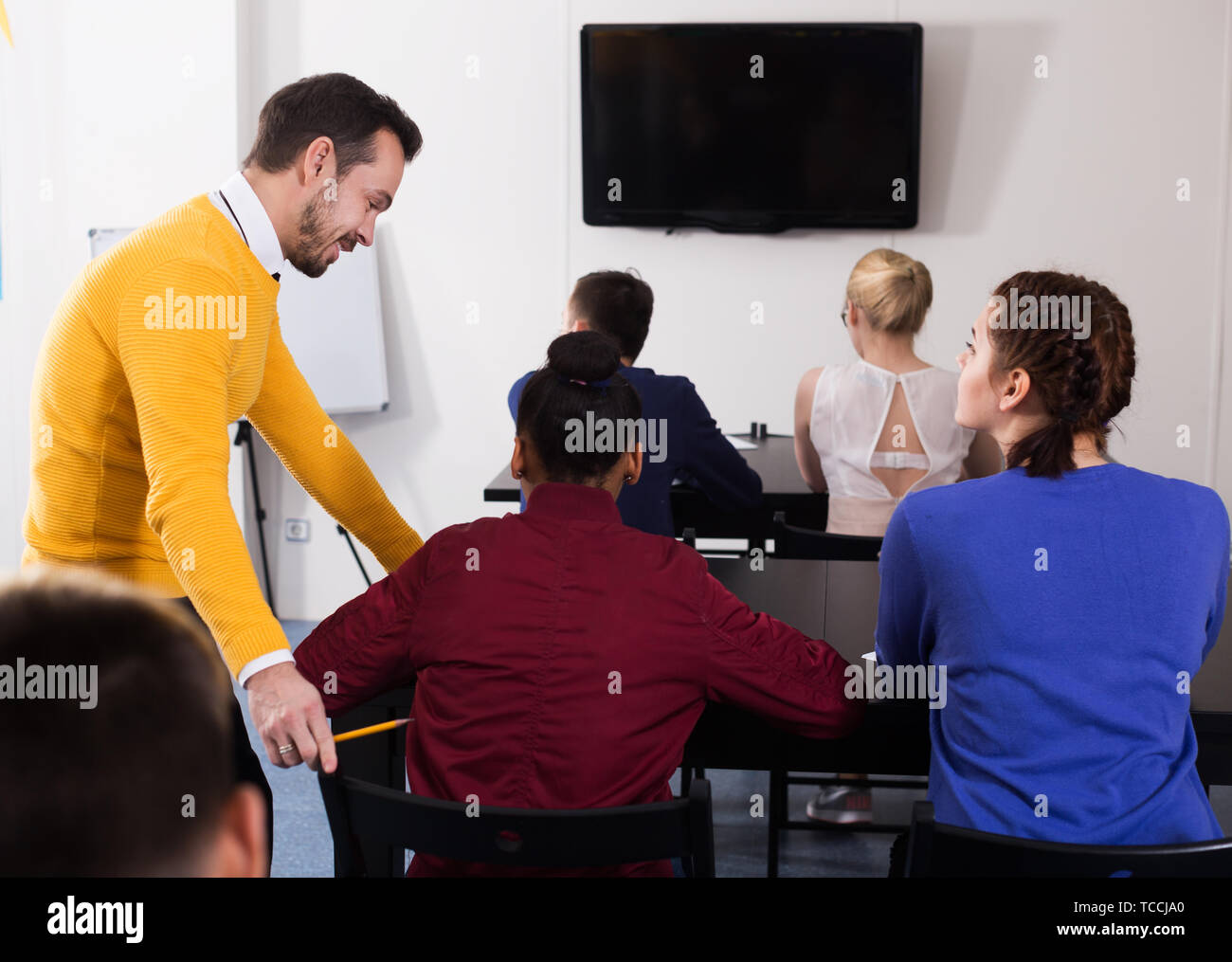 Sorridente insegnante per adulti dare spiegazione agli studenti durante il lavoro di revisione in classe Foto Stock