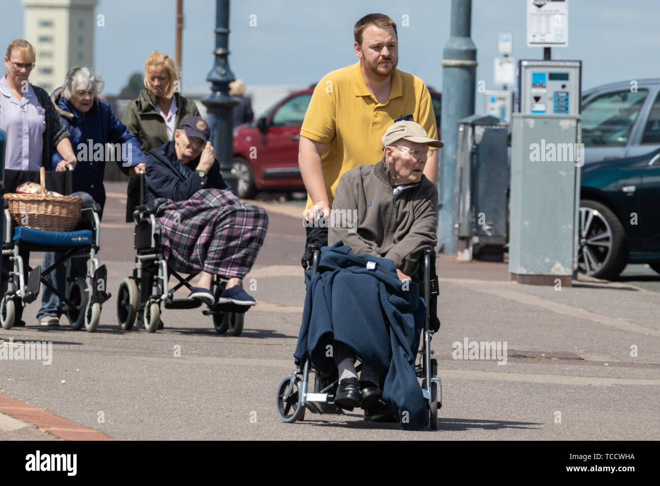 Una persona anziana essendo spinto in carrozzina da loro accompagnatore anziani aiutare da assistant Foto Stock
