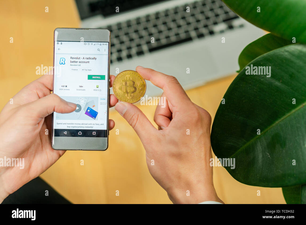 Lubiana, Slovenia 29.4.2019: imprenditore tenendo lo smartphone e cercando di scaricare app revolut e moneta Bitcoin su una scrivania in ufficio Foto Stock