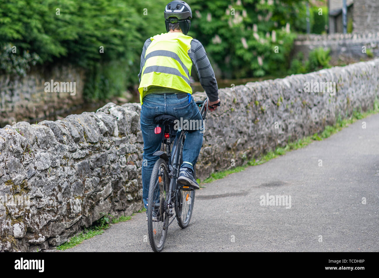Un maschio ciclista vanno in bicicletta in piena sicurezza marcia - casco, ad alta visibilità giacca, luci bici Foto Stock