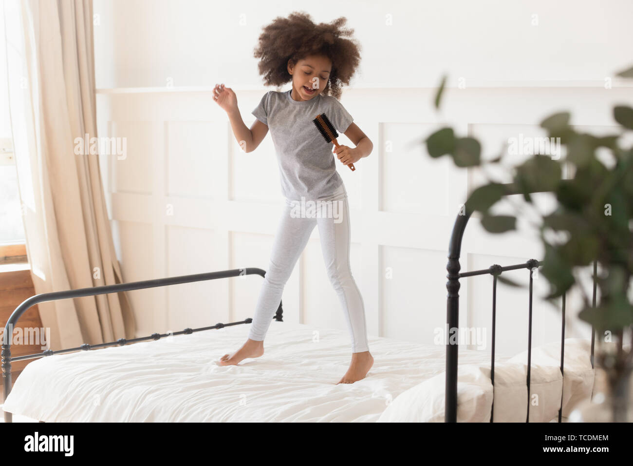 Divertenti capretto africano ragazza saltando su letto di cantare nella spazzola per capelli Foto Stock