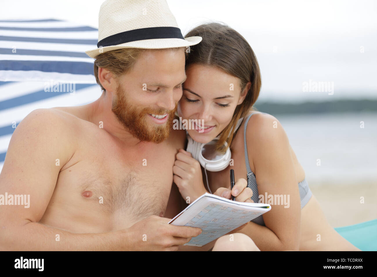 Coppia sulla spiaggia facendo cruciverba Foto Stock