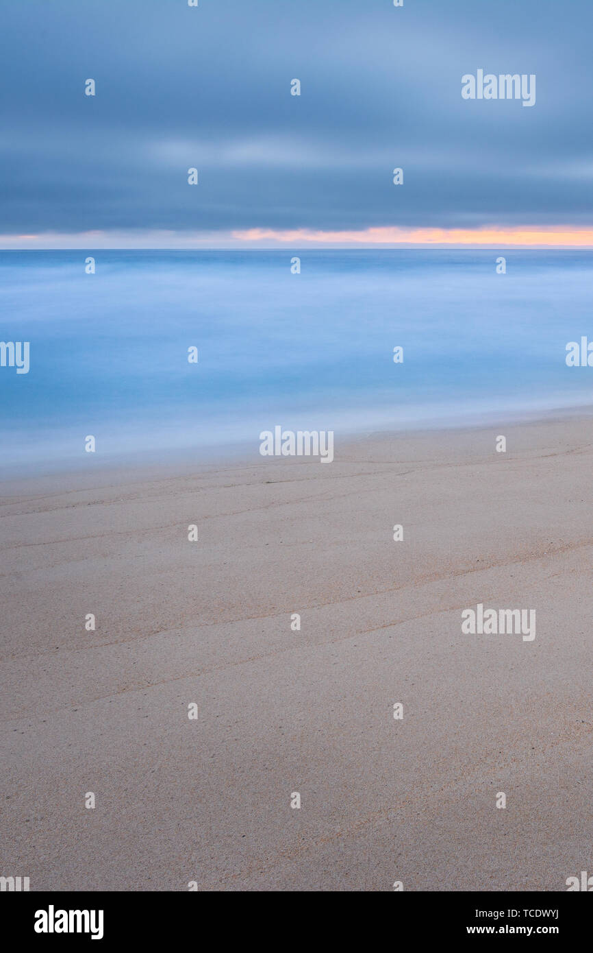 Sabbia chiara sulla spiaggia e la luce blu oceano in esposizione a lungo sotto il cielo nuvoloso Foto Stock