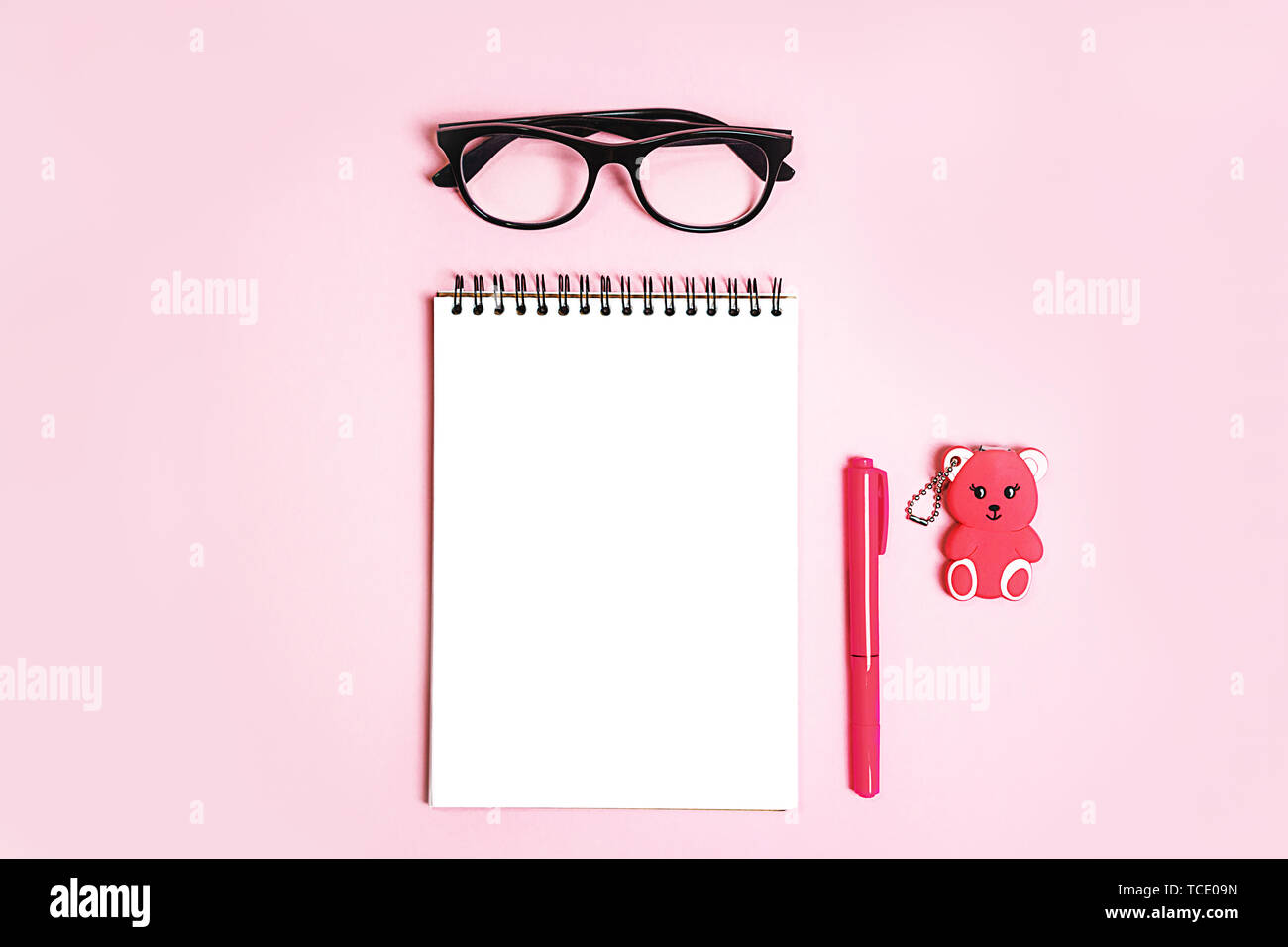 Blocco note con occhiali trendy e corallo rosa penna e orso giocattolo regalo pastello su sfondo rosa. Foto Stock