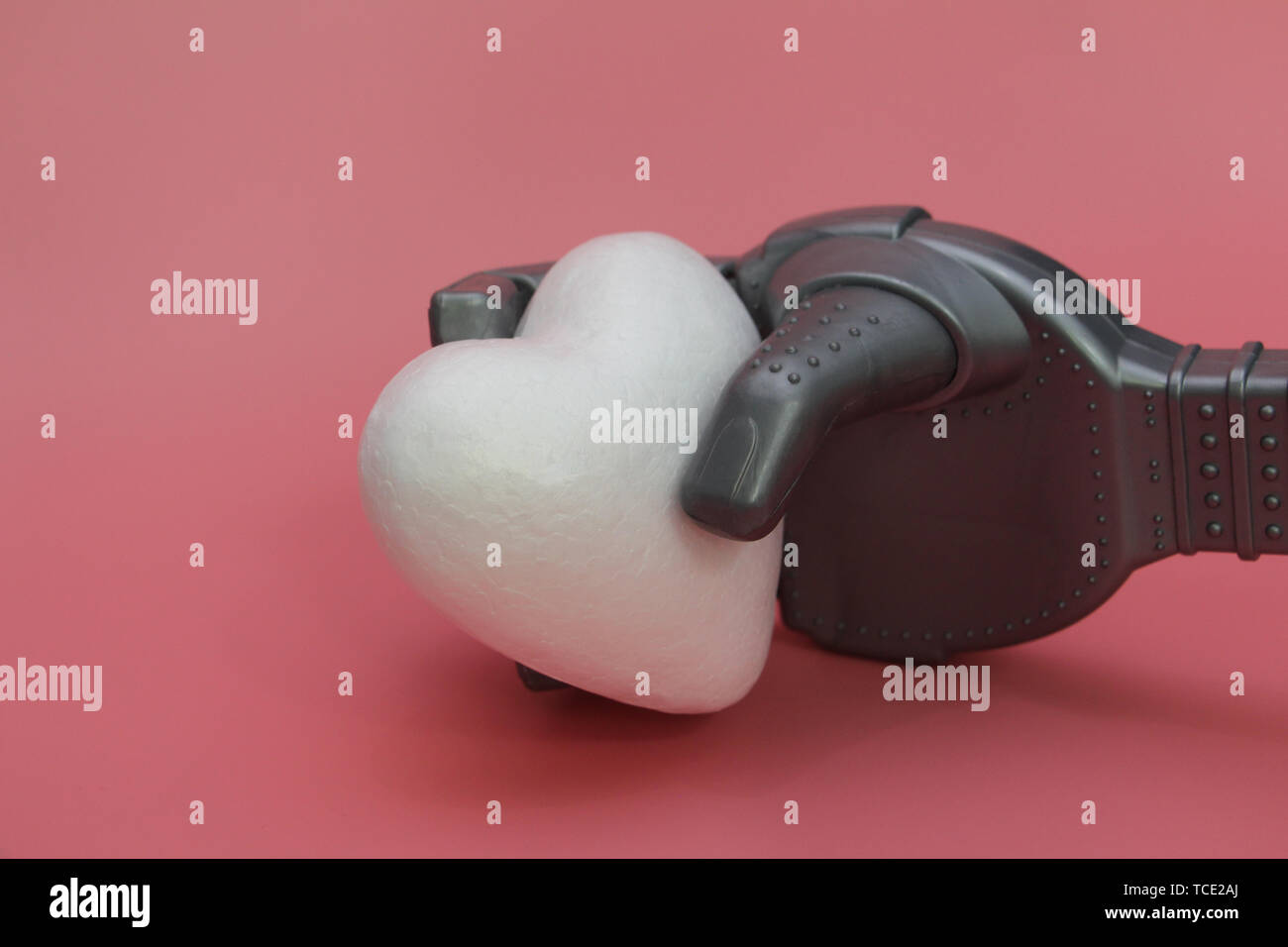 Il braccio di ferro di un robot tiene a cuore bianco. Concetto di robot con un cuore. Robot in medicina. Sfondo rosa. Foto Stock