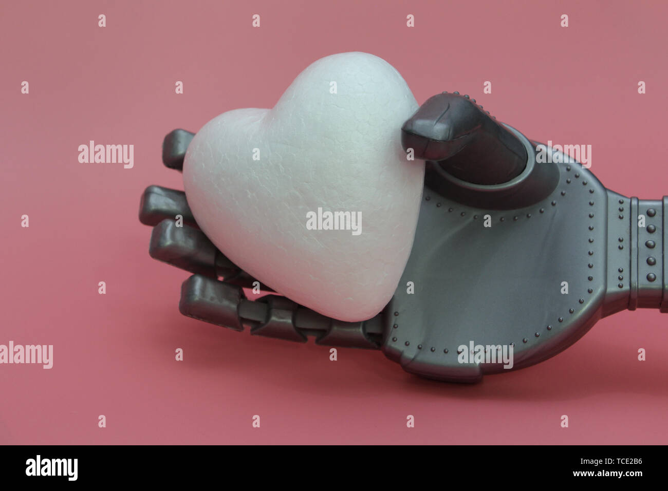 Il braccio di ferro di un robot tiene a cuore bianco. Concetto di robot con un cuore. Robot in medicina. Sfondo rosa. Foto Stock